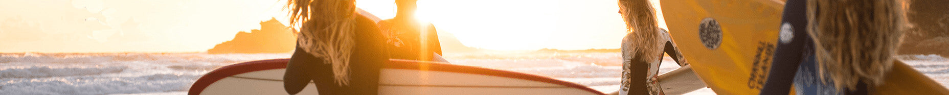 women in wetsuits on the beach carrying surfboards